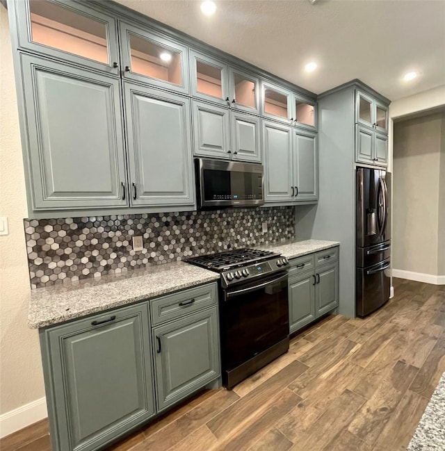 kitchen with stainless steel appliances, tasteful backsplash, light stone countertops, and light hardwood / wood-style floors