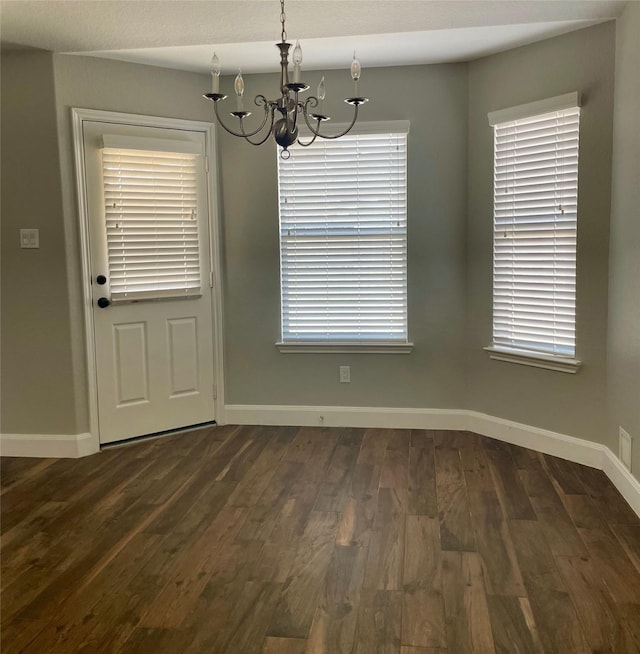 unfurnished dining area featuring dark wood-type flooring and a chandelier