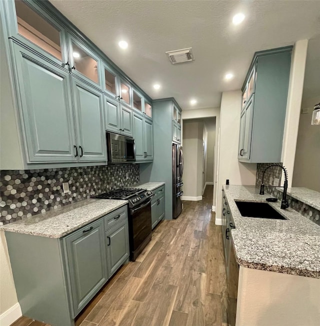 kitchen with tasteful backsplash, gas stove, light stone countertops, and sink