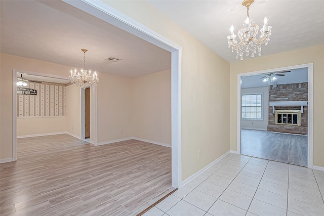 unfurnished dining area with a stone fireplace, ceiling fan with notable chandelier, and light hardwood / wood-style floors