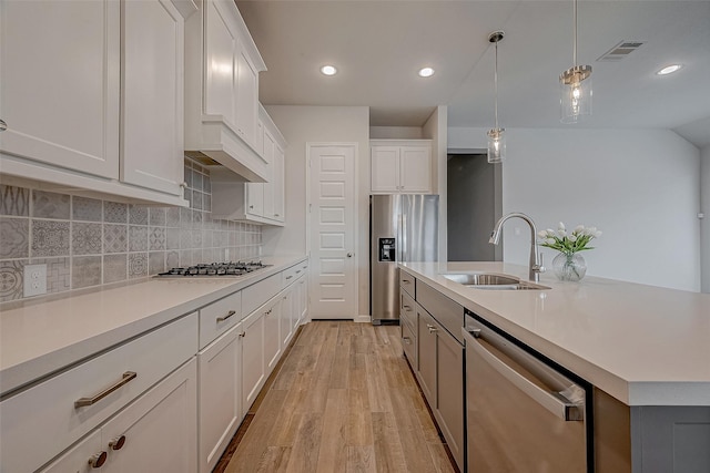 kitchen featuring sink, white cabinetry, hanging light fixtures, appliances with stainless steel finishes, and a kitchen island with sink