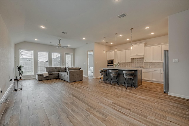 interior space featuring a breakfast bar, hanging light fixtures, appliances with stainless steel finishes, a kitchen island with sink, and white cabinets