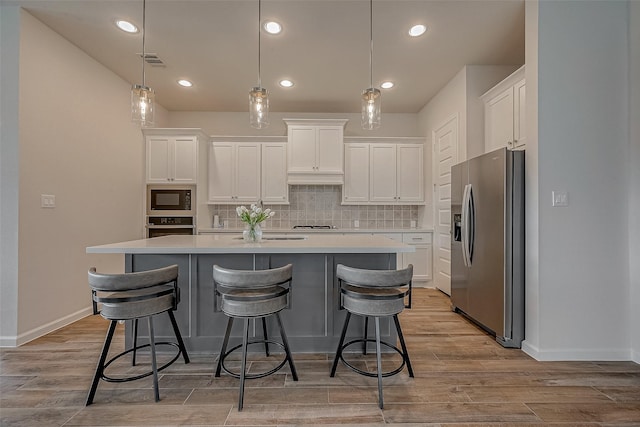 kitchen featuring built in microwave, oven, white cabinets, hanging light fixtures, and stainless steel refrigerator with ice dispenser