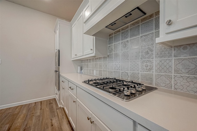 kitchen featuring wood finished floors, stainless steel appliances, premium range hood, white cabinetry, and backsplash