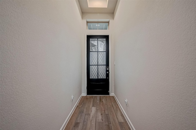 doorway with baseboards, wood finished floors, and a textured wall