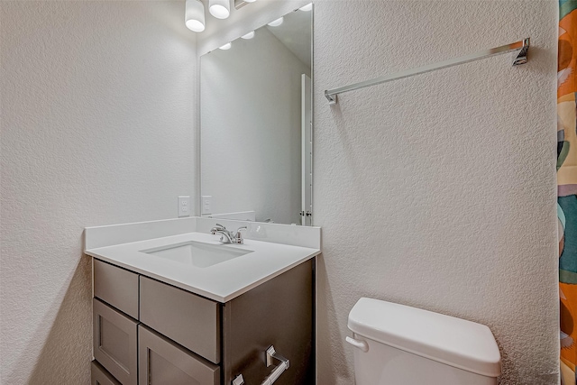 bathroom featuring toilet, a textured wall, and vanity