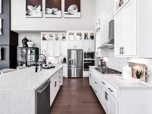 kitchen with wall chimney exhaust hood, sink, stainless steel appliances, light stone countertops, and white cabinets