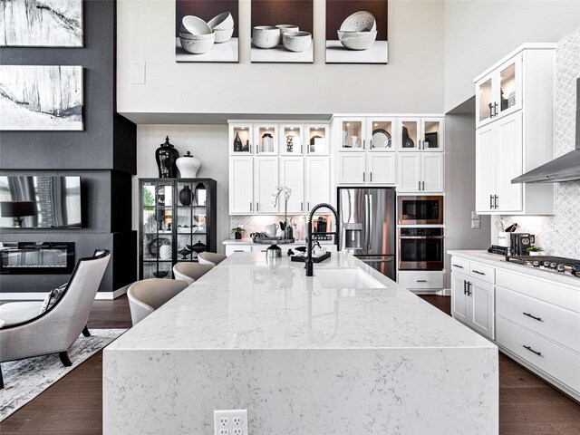 kitchen featuring sink, stainless steel appliances, light stone counters, white cabinets, and wall chimney exhaust hood