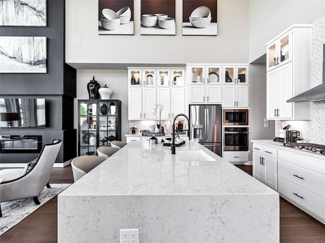 kitchen with sink, stainless steel appliances, light stone counters, white cabinets, and wall chimney exhaust hood