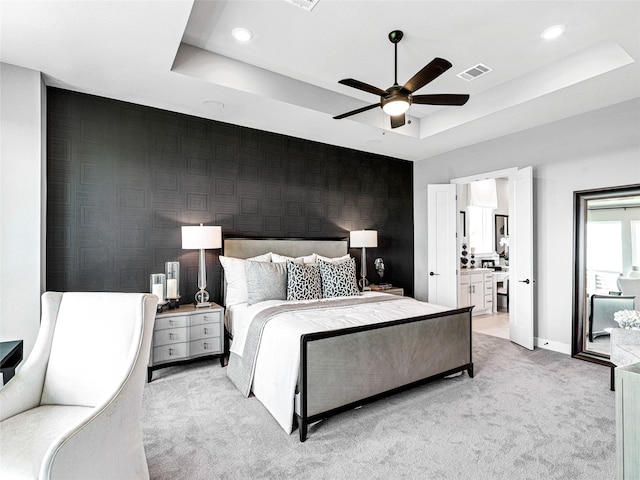 bedroom with ceiling fan, connected bathroom, a raised ceiling, and light carpet