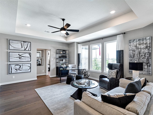 living room with dark wood-type flooring, a tray ceiling, and a textured ceiling