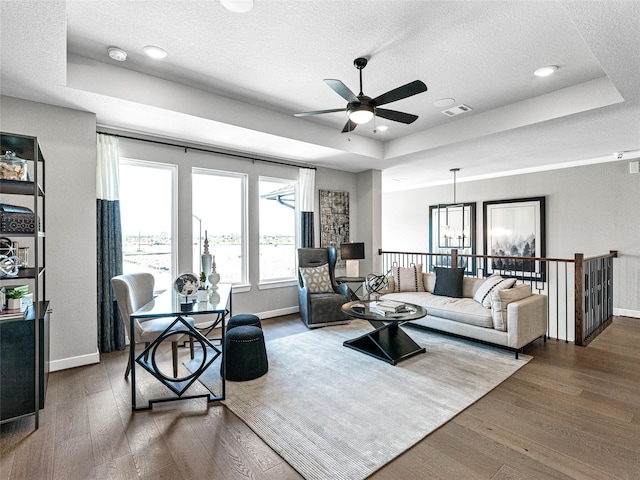 living room featuring dark wood-type flooring, ceiling fan, a raised ceiling, and a textured ceiling