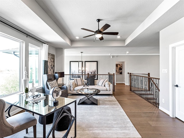 living room with a tray ceiling, a wealth of natural light, a textured ceiling, and hardwood / wood-style flooring