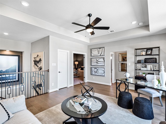 living room featuring dark hardwood / wood-style floors, ceiling fan, and a tray ceiling