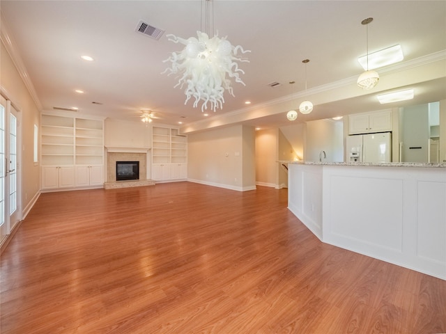 unfurnished living room featuring sink, crown molding, built in features, a fireplace, and light wood-type flooring