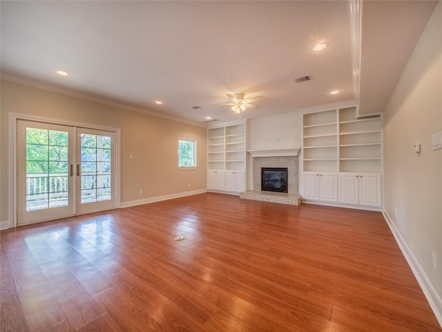 unfurnished living room featuring crown molding, light hardwood / wood-style flooring, ceiling fan, built in shelves, and french doors