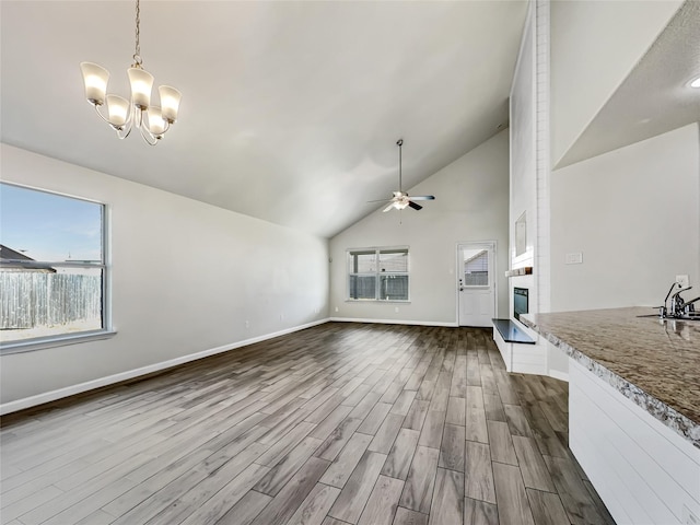 unfurnished living room with high vaulted ceiling, ceiling fan with notable chandelier, and dark hardwood / wood-style flooring