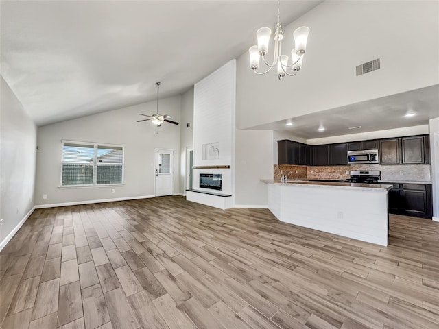 kitchen with light hardwood / wood-style flooring, a large fireplace, kitchen peninsula, stainless steel appliances, and backsplash