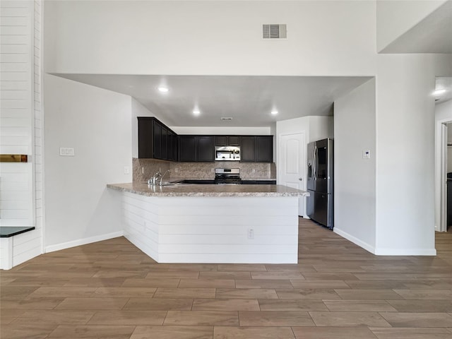 kitchen with tasteful backsplash, appliances with stainless steel finishes, kitchen peninsula, and light hardwood / wood-style flooring