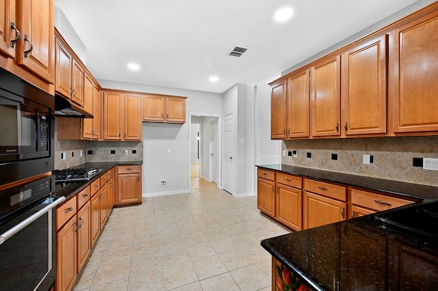 kitchen featuring dark stone countertops, backsplash, stainless steel gas cooktop, light tile patterned flooring, and oven