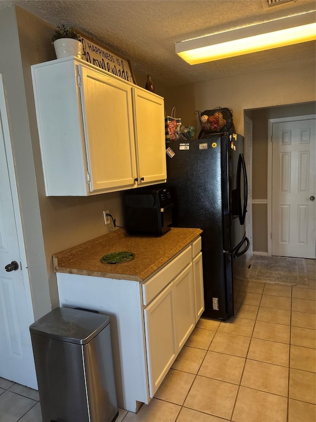 kitchen featuring black fridge with ice dispenser, light tile patterned floors, a textured ceiling, and white cabinets