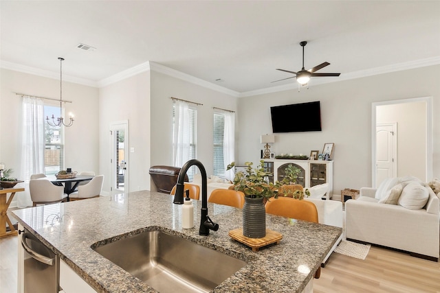 kitchen featuring sink, light hardwood / wood-style floors, decorative light fixtures, stainless steel dishwasher, and dark stone counters