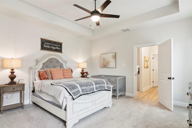 bedroom featuring ceiling fan, a tray ceiling, and light carpet