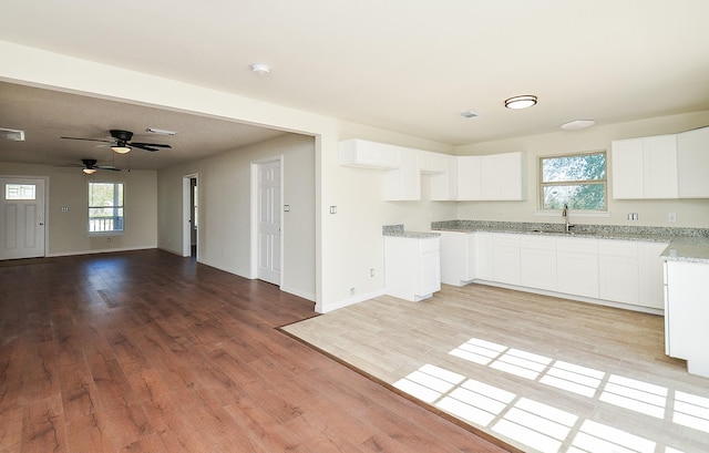 kitchen with sink, white cabinets, ceiling fan, light hardwood / wood-style floors, and light stone countertops