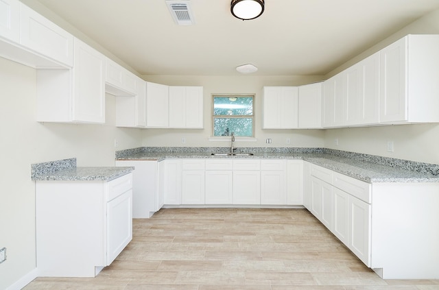 kitchen with white cabinetry, light stone countertops, sink, and light hardwood / wood-style flooring