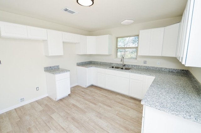 kitchen featuring white cabinetry, sink, light stone countertops, and light wood-type flooring