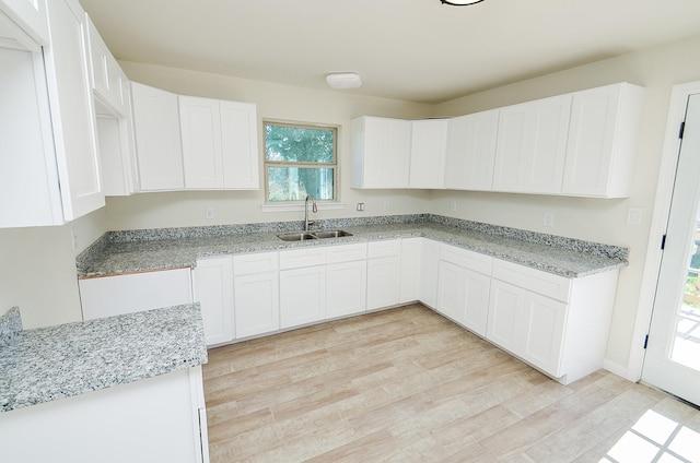 kitchen with white cabinetry, light stone countertops, sink, and light hardwood / wood-style floors