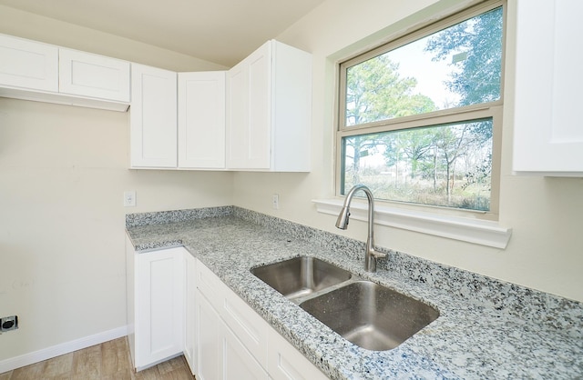 kitchen featuring white cabinetry, sink, light stone countertops, and light hardwood / wood-style floors