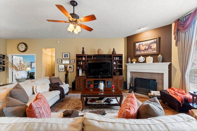 living room with hardwood / wood-style flooring, a tile fireplace, ceiling fan, and a textured ceiling