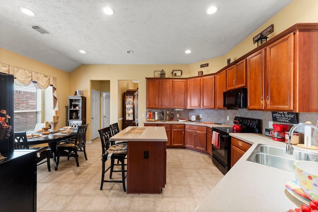 kitchen with sink, tasteful backsplash, a center island, a kitchen breakfast bar, and black appliances