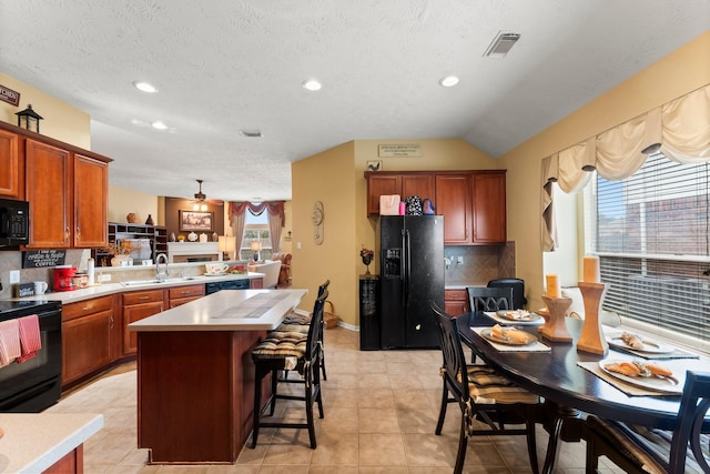 kitchen featuring sink, a breakfast bar area, a center island, black appliances, and decorative backsplash