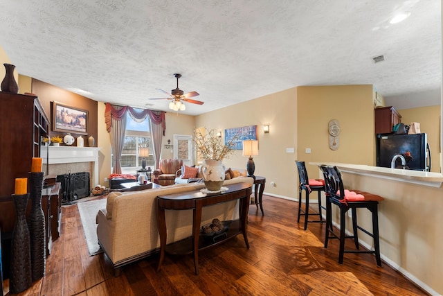 living room featuring a tiled fireplace, ceiling fan, dark hardwood / wood-style floors, and a textured ceiling