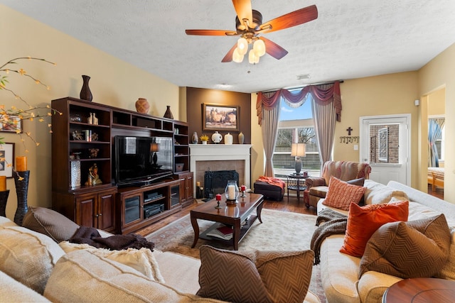 living room with hardwood / wood-style flooring, ceiling fan, a tile fireplace, and a textured ceiling