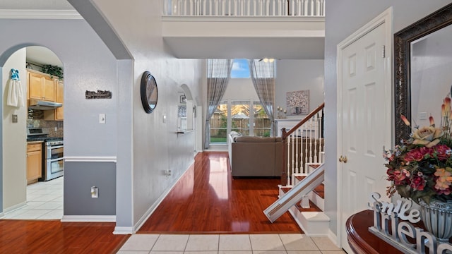 foyer entrance featuring crown molding, baseboards, stairs, light tile patterned floors, and arched walkways