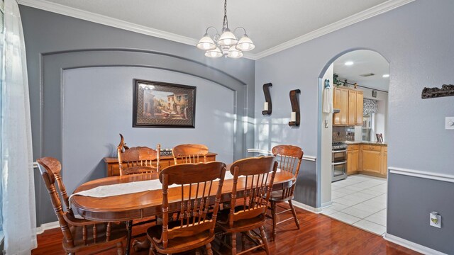 dining space with a notable chandelier, ornamental molding, arched walkways, light wood-style floors, and baseboards