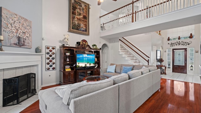 living room featuring hardwood / wood-style flooring, ceiling fan, a towering ceiling, and a fireplace