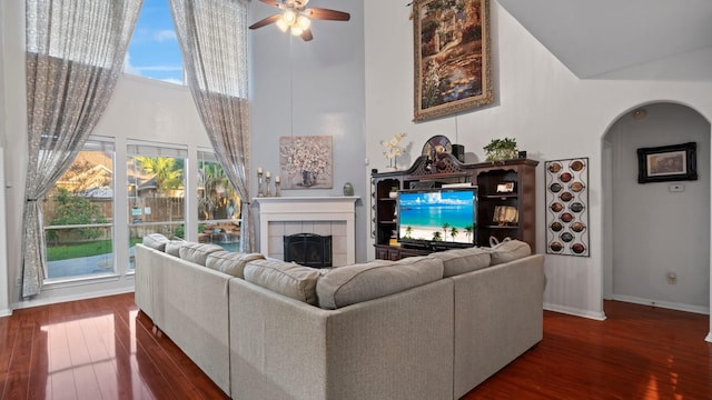 living area featuring a fireplace, a high ceiling, wood finished floors, arched walkways, and a ceiling fan