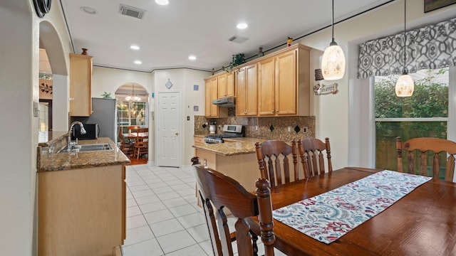 kitchen with tasteful backsplash, under cabinet range hood, arched walkways, gas stove, and a sink