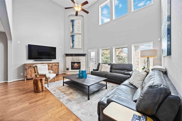 living room with a fireplace, ceiling fan, and light wood-type flooring