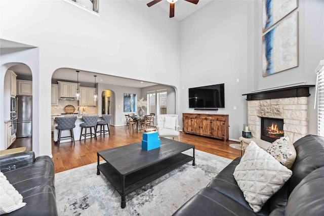 living room featuring ceiling fan, wood-type flooring, a fireplace, and a high ceiling