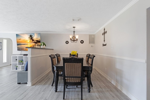 dining room with ornamental molding, light hardwood / wood-style floors, a chandelier, and a textured ceiling