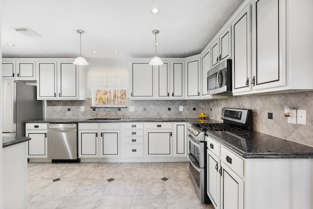 kitchen with stainless steel appliances, dark stone counters, pendant lighting, sink, and white cabinetry