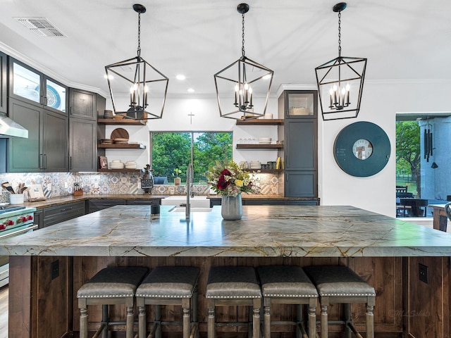 kitchen featuring high end stainless steel range, tasteful backsplash, ornamental molding, pendant lighting, and a large island