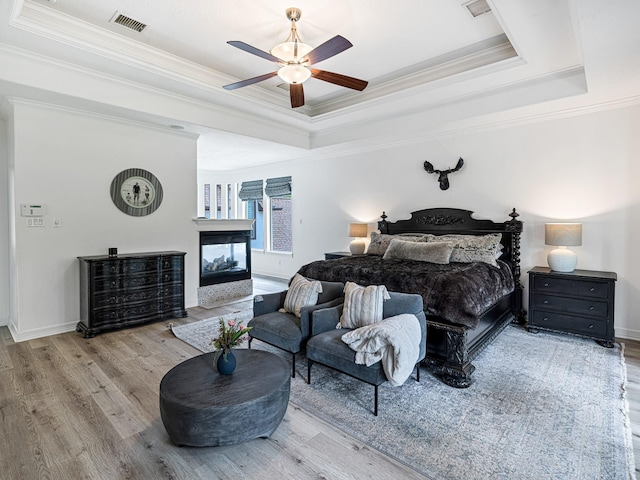 bedroom with crown molding, a multi sided fireplace, a tray ceiling, and light hardwood / wood-style floors