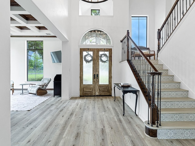 entryway featuring french doors, a towering ceiling, coffered ceiling, and light wood-type flooring