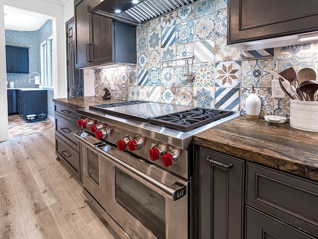 kitchen featuring wall chimney range hood, double oven range, dark brown cabinetry, light hardwood / wood-style floors, and decorative backsplash